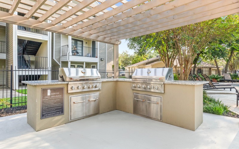 Outdoor grilling station with stainless steel gas grills and shaded pergola beside the pool at Baton Rouge apartments.