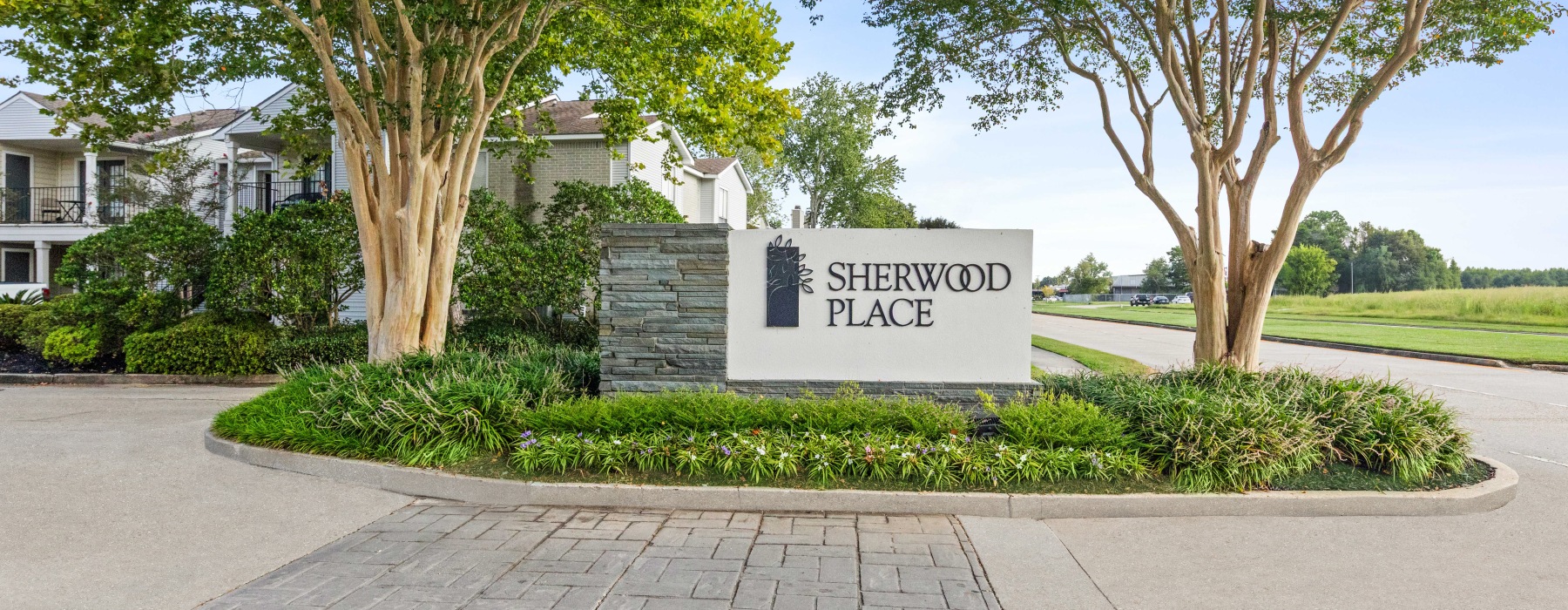 Entrance sign for Sherwood Place Apartments framed by landscaped greenery and tall trees in East Baton Rouge.